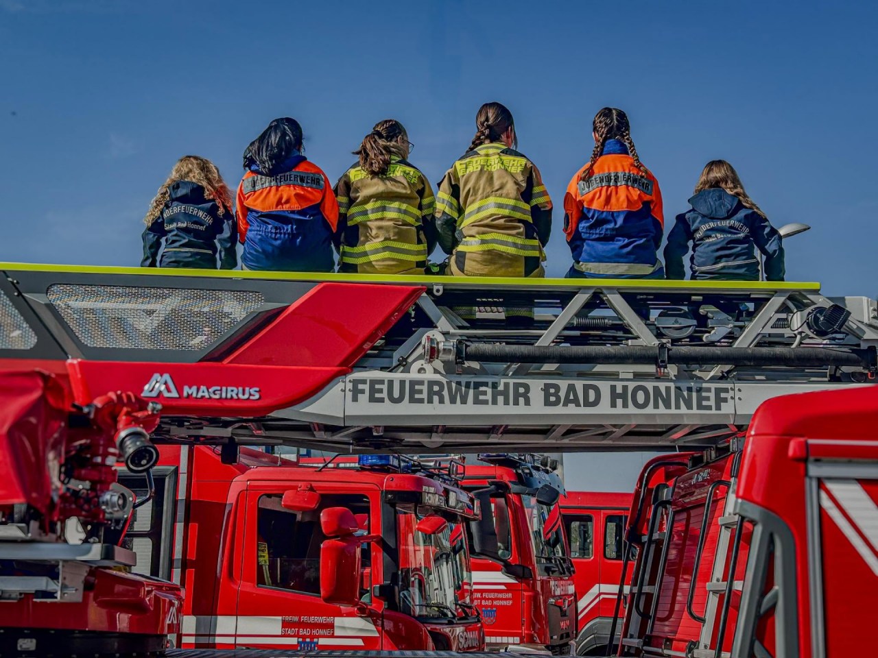 Feuerwehrfrauen und Nachwuchskräfte der Feuerwehr Bad Honnef sitzen auf der Drehleiter über den Einsatzfahrzeugen